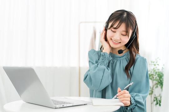 A young Asian businesswoman working in front of her computer, wearing a headset.