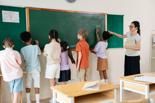 Group of diverse young kid students drawing on green board in classroom. 