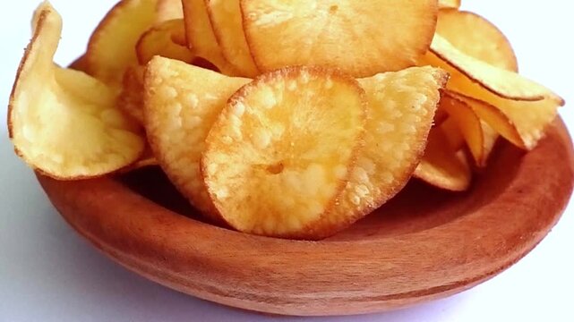 close-up of rotating cassava chips served on a wooden bowl with a white background