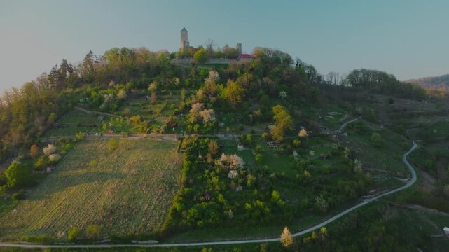 Aerial ascending tilt-up shot showing Starkenburg Castle atop green hillside in Heppenheim at sunset, Germany