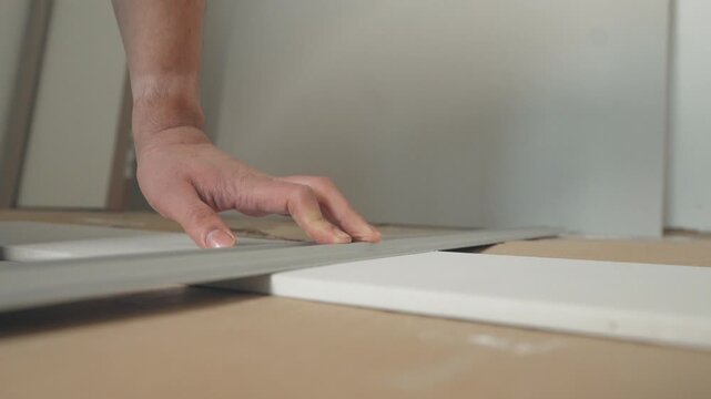 Close-up of hands using a utility knife to cut along white flat-pack furniture panels on cardboard