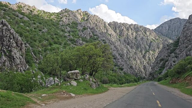 A winding road cuts through a dramatic mountain canyon, towering rocky peaks rising on both sides beneath a bright blue sky scattered with clouds
📍 Darbabd dezli, Sarvabad, Kurdistan 