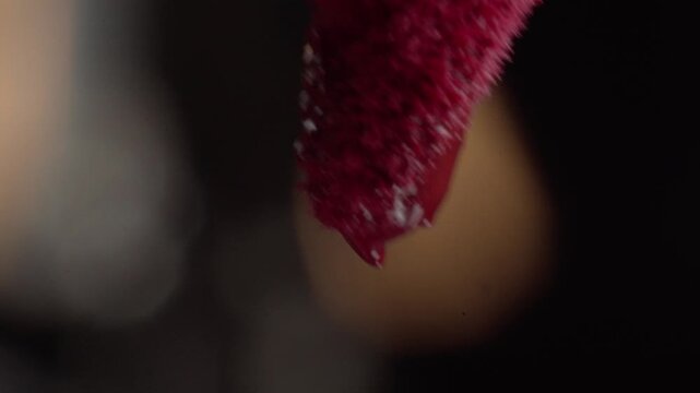 Macro close up of red cosmetic applicator with textured surface and liquid droplet forming at the tip against dark blurred background with soft focus