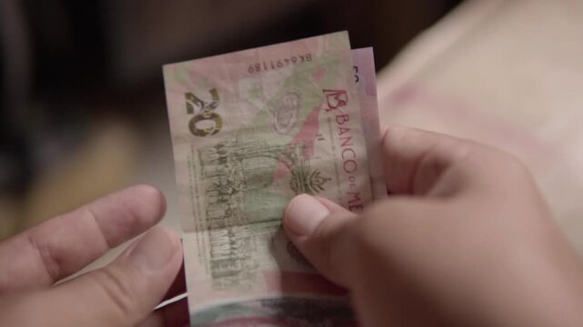 Hands counting Mexican peso banknotes, showing several fifty peso denominations held between fingers, with printed details and currency texture visible in close up view