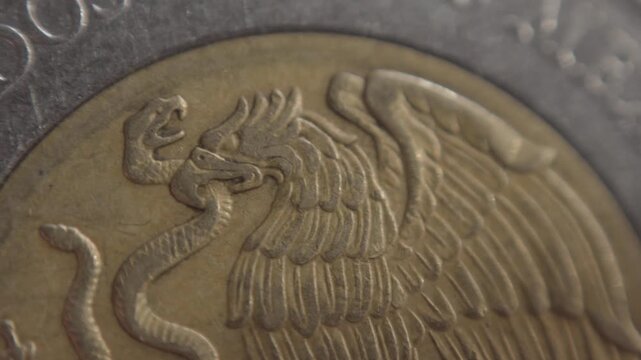 Macro close up of Mexican coin featuring detailed eagle emblem, raised metal engraving and textured surface, highlighting national currency design and fine minting detail