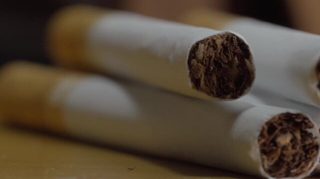 Close up showing cigarettes with exposed tobacco ends revealing rolled tobacco leaves and fine paper texture against a softly blurred dark background