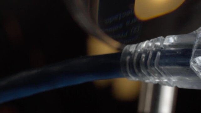 Close up macro view of transparent Ethernet cable connector with plug, visible metal contacts, internal wires and plastic housing against dark blurred background.
