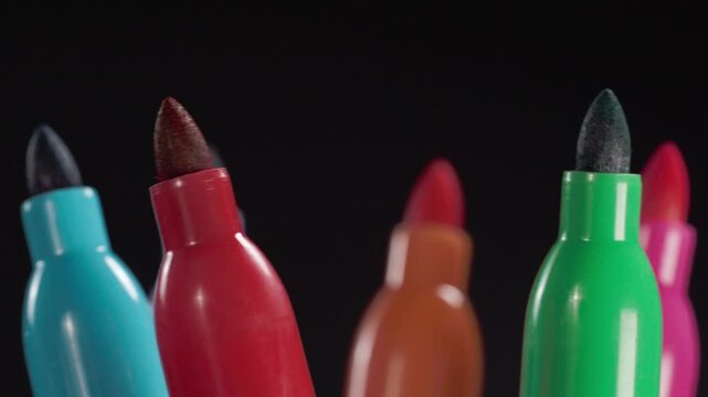 Close up of colorful felt tip markers with red, purple, green, orange and pink tips arranged against black background, highlighting varied shapes and vibrant colors