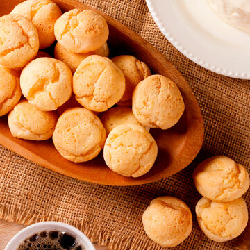 Homemade Brazilian cheese bread served on a wooden platter, accompanied by fresh Minas cheese, butter, and black coffee