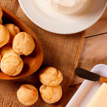 Homemade Brazilian cheese bread served on a wooden platter, accompanied by fresh Minas cheese, butter, and black coffee