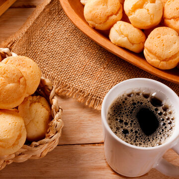 A cup of black coffee accompanied by homemade cheese bread, served in a natural fiber basket on a rustic wooden table.