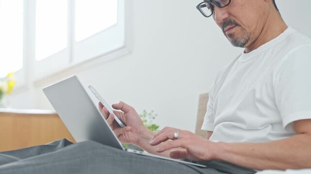 ベッドでノートPCを使うシニア男性。パソコン、仕事、DX、スマホ、アプリ、ワーケーション、テレワーク