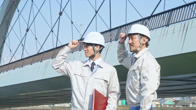 橋の前に立つ男性作業員のグループ。インフラ、工事、建設、点検、検査、橋梁、エンジニア、保守、業者