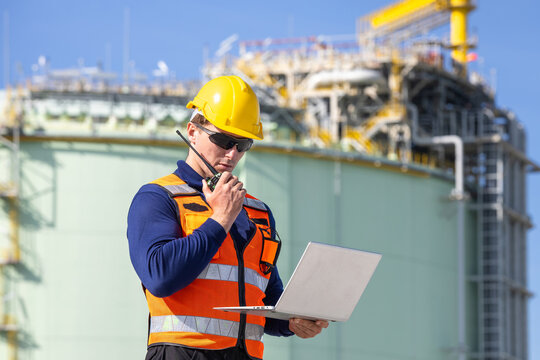 lng plant engineer with laptop and walkie talkie at terminal, liquefied natural gas worker using radio and computer at facility, energy industry professional inspecting natural gas storage tanks