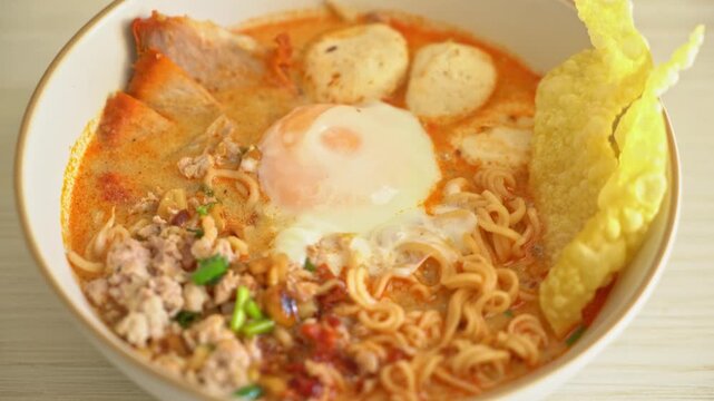 Bowl of spicy tom yum instant noodles with egg and pork on table.