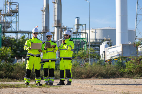 oil refinery engineers working with laptop and tablet at plant, petroleum plant team using digital devices and radio outdoors, energy industry professionals inspecting industrial facility site