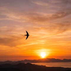 Fototapeta premium Silhouette of a swift bird flying gracefully across a vibrant sunset sky over a calm body of water and distant mountains.