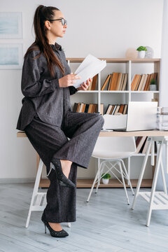 Office career. Manager paperwork. Pensive female professional reviewing business document at desk with laptop at modern workplace.