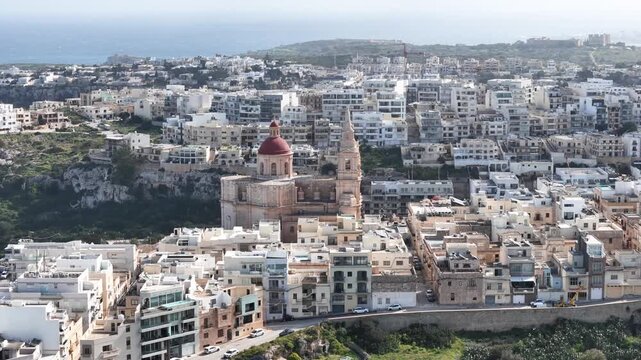 mellieha parish church red dome bell tower hilltop overlooking whitewashed town rooftops mediterranean sea horizon aerial drone orbit malta religious landmark historic architecture hillside cliffs