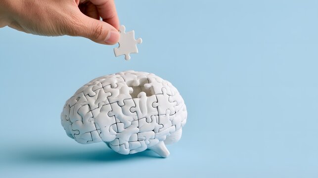 Hand placing the last jigsaw puzzle piece into a white brain model, mental health, memory care, problem solving, psychology, neuroscience, dementia awareness and completing the thinking process