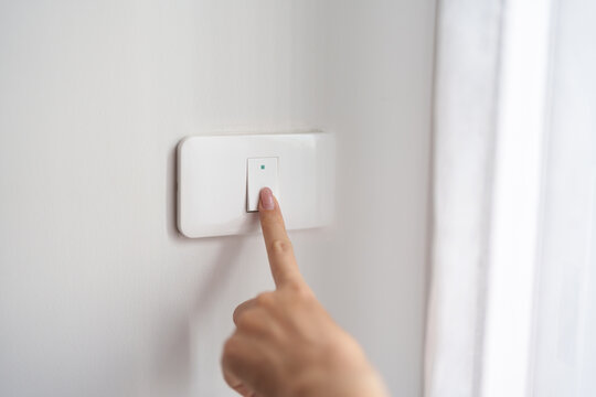 Female finger pushing for turn on light switch on white wall at home room. Woman hand turn off lighting Switch. Energy Saving, energy power control, electrical, eco environment, and lifestyle concept