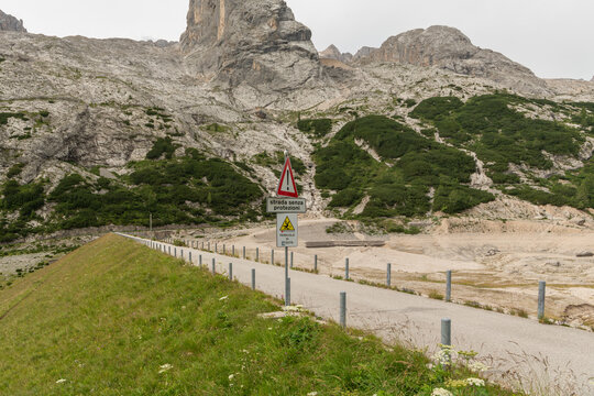 Lago di Fedaia, Italy. Warning road sign and exposed reservoir landscape showing drought and low water levels in the Italian Alps