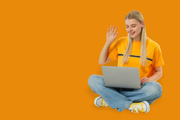 Freelancer. Young woman sits cross-legged with laptop, waving and smiling © Atlas