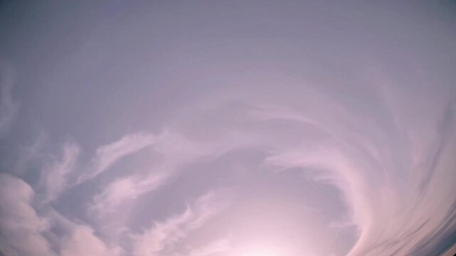 Watching soft pink clouds swirling across a purple sky as warm sunlight shines over the tranquil heavens while peaceful vapor forms gentle concentric rings across the beautiful high firmament
