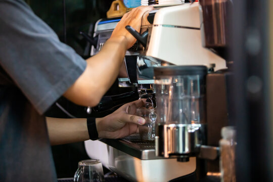 Selective focus to Side view of a barista operating a commercial espresso machine to extract a fresh coffee shot into a glass at a modern cafe counter.