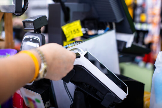 Selective focus to customer tapping a credit card on a POS terminal at a cashier counter for contactless payment in a retail store.