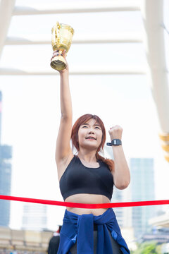 A beautiful, fit woman holds a victory trophy in the middle of the city; a concept promoting health.