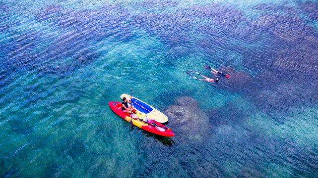 Top aerial view of Group of tourist are enjoy on water sport paddle sup-board with kayaking along at the edge of the sea beach under crystal clear of water in the island of summer trip