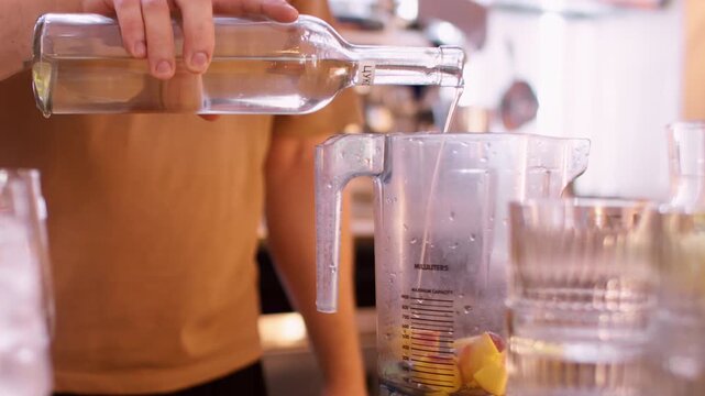 Cocktail recipe. Syrup smoothie. Male barkeeper pouring liquor from bottle in blender with peach pieces. Fresh aroma juice ingredient.