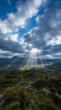 Sunbeams breaking through dramatic clouds over a vast mountain landscape.