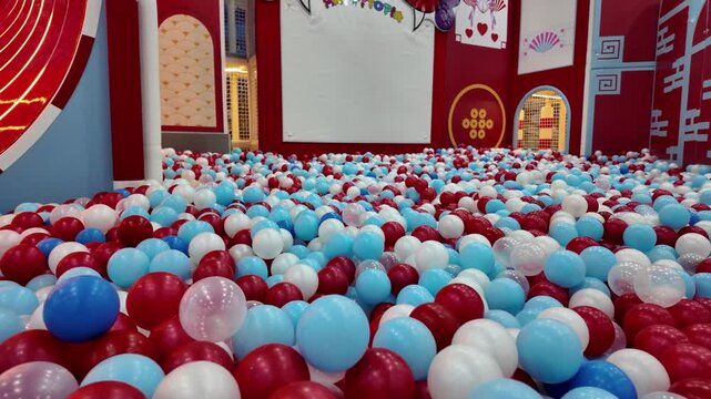 Large colorful ball pit filled with red blue and white plastic balls in an indoor children playground.