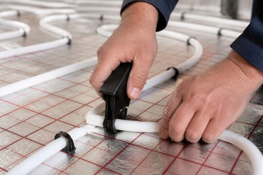Worker fastening pex tubing on insulated floor grid