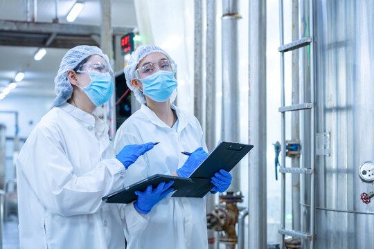 Food processing quality control inspectors checking factory facility, Female factory workers in protective gear with clipboard and tablet at plant discussing production at facility