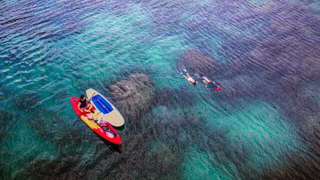 Top aerial view of Group of tourist are enjoy on water sport paddle sup-board with kayaking along at the edge of the sea beach under crystal clear of water in the island of summer trip