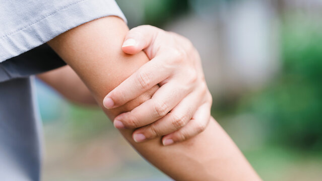 Close-up of an adult man holding his painful forearm and elbow outdoors. He is suffering from acute muscle strain, joint stiffness, and physical discomfort. Healthcare and medical pain concept.