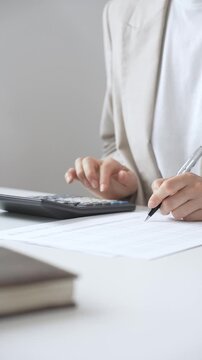 Businesswoman is calculating annual tax using calculator and taking notes in the office, managing domestic budget and checking financial documents. Audit and taxes in business