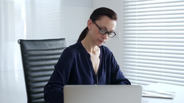 Professional businesswoman wearing glasses, working with papers and laptop at modern workspace, embodying corporate diligence and focused work performance. Business people concept