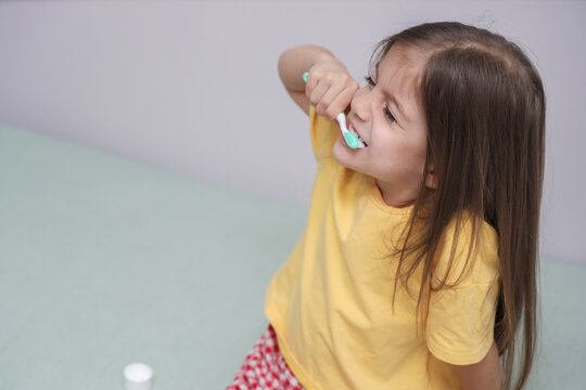 Small Child In Yellow Shirt Brushes Teeth With Focused Expression, Holding Toothbrush Near Mouth In Bright Indoor Setting. Additional Visual Context For, With Child, Tooth, Brushing, Teeth Detail