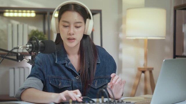 Podcast digital creator home studio microphone headphone female recording voice at tidy desk with laptop and mixer, focused live audio session, mixing, typing, producing content with warm lamp light