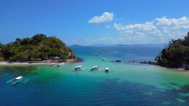 Tropical bay with clear turquoise water and traditional Filipino bangka boats. Relaxing summer vacation in a stunning natural landscape. Dramatic aerial view static hovering drone panorama
