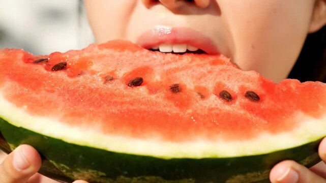 Close up of a child eating watermelon slice in summer light