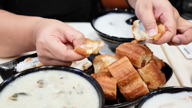 Hands Breaking Fried Dough Sticks Over Bowls of Congee
