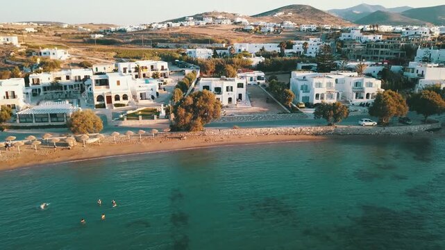Aerial view of sunny greek island coastline with luxury villas and swimming people in turquoise sea.