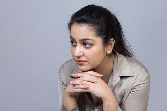 Portrait of an Young Indian woman sitting and looking away with a sad and thoughtful expression, portraying loneliness, emotional distress, disappointment, and introspection isolated on gray studio