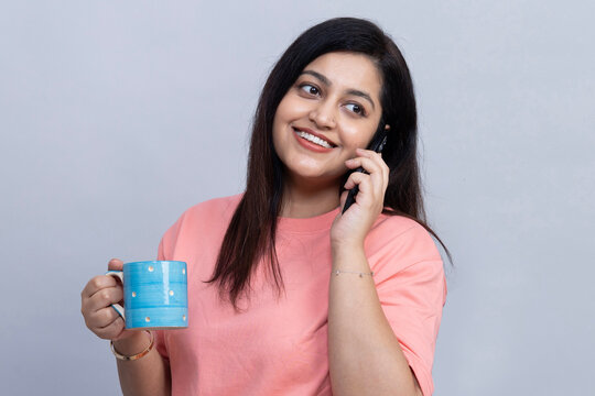 Cheerful indian young woman enjoying a phone conversation while holding a blue mug, representing modern communication, social connection, leisure, and a relaxed lifestyle.