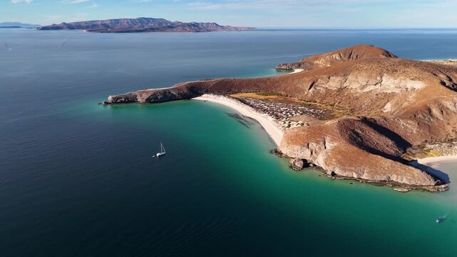 Aerial shot of calm turquoise cove and rocky coastline with sailboat anchored in La Paz Mexico
